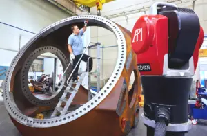 A worker stands on a ladder inside a large circular metal gear in an industrial workshop.