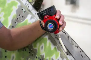 Close-up of a hand holding a red laser distance meter next to a metal measuring ruler on a perforated steel beam.