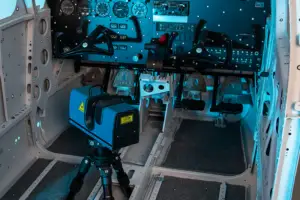 Inside an aircraft cockpit, a tripod-mounted camera sits on the floor beside the flight controls and instrument panels.