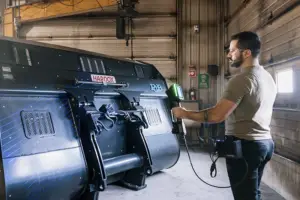 Technician using handheld XRF analyzer to test Hardox steel material on industrial equipment in workshop.