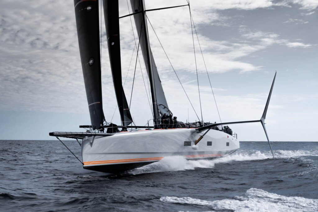 High-performance racing sailing yacht with black sails and crew cutting through ocean waves at speed.