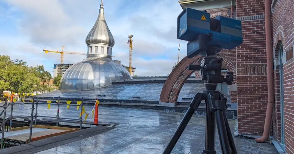 3D laser scanner on tripod documenting silver onion dome and brick architecture during historic building restoration